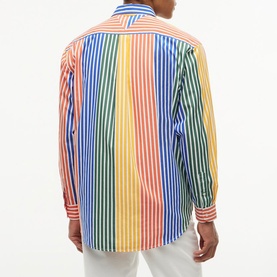 Model wearing Tommy Hilfiger multicolour striped shirt in orange, blue, green, yellow and red vertical stripes, back view, styled with white trousers.