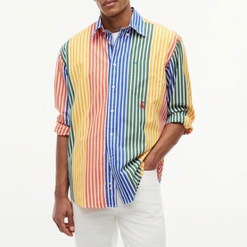 Model wearing Tommy Hilfiger multicolour stripe shirt in orange, blue, yellow and green with white trousers