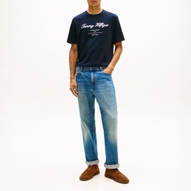 Model wearing navy Tommy Hilfiger graphic T-shirt with script logo, styled with mid-wash straight jeans and brown suede loafers