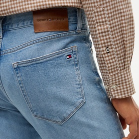 Model wearing Tommy Hilfiger Rio Blue jeans, close-up of back pocket with logo flag, styled with a brown gingham shirt.