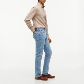 Model wearing Tommy Hilfiger jeans in Rio Blue, straight leg fit, styled with a beige shirt and brown leather shoes.
