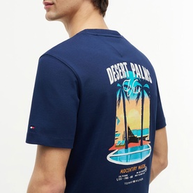 Model wearing Tommy Hilfiger Carbon Navy t-shirt, back view showing Desert Palms graphic print with sunset scene.