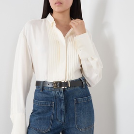 Model wearing Victoria Beckham Dorian Pin Buckle Belt in black grained leather with gold-tone hardware, styled with cream blouse and blue jeans.