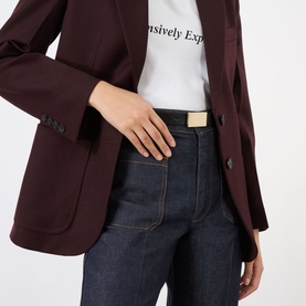 Model wearing Victoria Beckham Portofino Mirror Leather Belt in black with gold-tone hardware, styled with dark jeans and burgundy blazer.