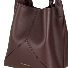 Victoria Beckham Victoria Bucket Bag in dark burgundy leather, close-up showing angular panel detail, top carry handle and gold-foil logo lettering
