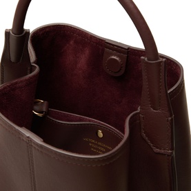 Victoria Beckham Victoria Bucket Bag in dark burgundy leather, open top view showing burgundy suede lining and gold-foil logo, magnetic closure