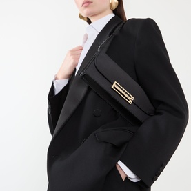 Model carrying Victoria Beckham Dorian East West Clutch in black satin with gold-tone B-buckle hardware, styled with an oversized black blazer