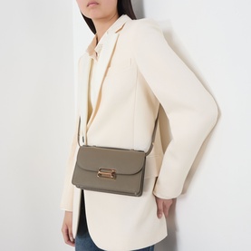 Model carrying Victoria Beckham Dorian Small Shoulder Bag in Fossil Brown, gold-toned hardware, worn crossbody over cream blazer.