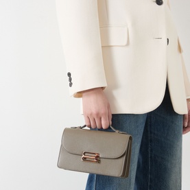 Model carrying Victoria Beckham Dorian Small Shoulder Bag in Fossil Brown, gold-toned hardware, top handle, styled with cream blazer and jeans
