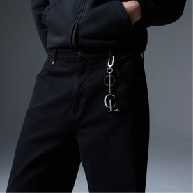 Christian Louboutin silver CL logo charm keyring attached to black jeans waistband, with black hoodie styled alongside.