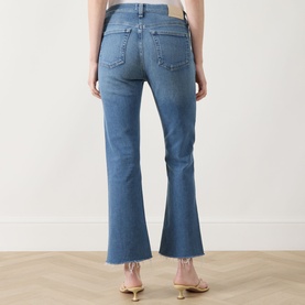 Model wearing Citizens of Humanity Goldie Ankle Kick Flare Jeans in Calla, showing rear view with raw hems and logo badge. Styled with gold heeled
