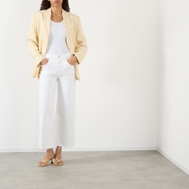 Model wearing Citizens of Humanity Lyra High-Rise Cropped Wide Leg Jeans in Soft White with frayed hem, styled with a cream blazer and tan heeled