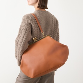 Model carrying Coach Kisslock Large Frame Bag in Amber Brown leather, gold-tone hardware and shoulder strap, styled with a cable-knit sweater