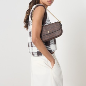 Model carrying Coach Brooke Chain Crossbody Bag in Maple, C-logo coated canvas with gold-tone chain strap, styled with plaid vest and white trousers