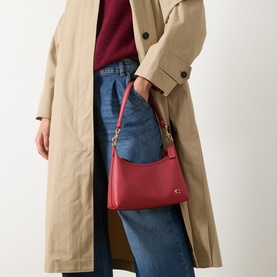 Model carrying Coach Juliet 25 Leather Shoulder Bag in Poppy red with gold-tone hardware, styled with beige trench coat and blue jeans