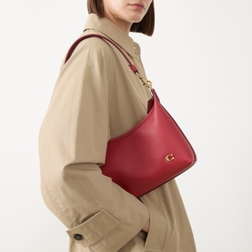 Model carrying Coach Juliet 25 Leather Shoulder Bag in Poppy red with gold-tone logo hardware, styled with a beige trench coat