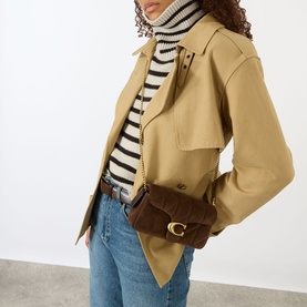 Model carrying Coach Tabby 19 Quilted Suede Crossbody Bag in Dark Chocolate with gold-toned hardware, styled with trench coat and striped knit