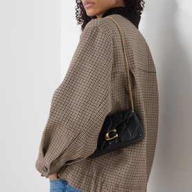 Model carrying Coach Tabby 19 Quilted Crossbody Bag in black leather, gold-tone chain strap and C-logo detail, styled with a houndstooth jacket