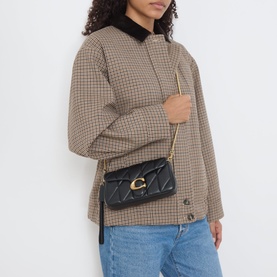 Model carrying Coach Tabby 19 Quilted Crossbody Bag in black with gold-tone hardware and chain strap, styled with houndstooth jacket and jeans