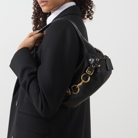 Model carrying Coach Ergo 26 Belted Shoulder Bag in black leather with gold-tone hardware, styled with a black blazer and white shirt.