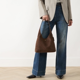 Model carrying Coach Brooklyn 28 Suede Shoulder Bag in Dark Chocolate with gold-toned hardware, styled with wide-leg jeans and blazer.