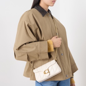 Model carrying Coach Tabby 19 Quilted Crossbody Bag in Chalk with gold-toned chain strap and metal C monogram, styled with a tan jacket