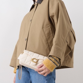 Model carrying Coach Tabby 19 Quilted Crossbody Bag in Chalk with gold-toned hardware, styled with a tan jacket and jeans.