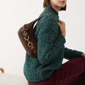 Model carrying Coach Ergo 26 Belted Suede Shoulder Bag in dark chocolate with gold-tone hardware, worn over shoulder, styled with green knit jumper.