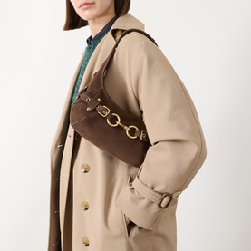 Model carrying Coach Ergo 26 Belted Suede Shoulder Bag in Dark Chocolate with gold-tone hardware, styled with a beige trench coat