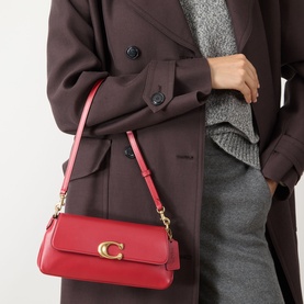 Model carrying Coach Jet Shoulder Bag in Poppy red leather, gold-toned C hardware, worn over shoulder, styled with dark oversized coat