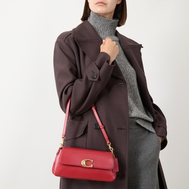 Model carrying Coach Jet Shoulder Bag in Poppy red leather, gold-toned C hardware, detachable strap, styled with dark coat and grey knitwear.