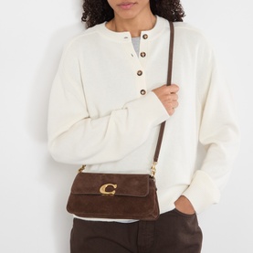 Model carrying Coach Jet Suede Shoulder Bag in Dark Chocolate with gold-tone C hardware and adjustable strap, styled with cream sweatshirt