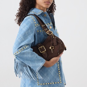 Model carrying Coach Drifter Small Shoulder Bag in dark chocolate suede with gold-tone hardware, buckle detail and padlock charm, styled with a