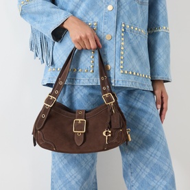 Model carrying Coach Drifter Small Shoulder Bag in dark chocolate suede, gold-tone hardware, buckle strap and keychain charm, styled with blue denim