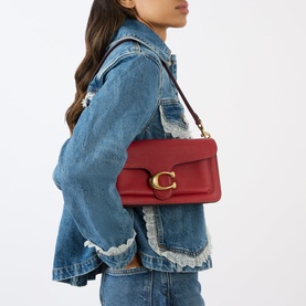 Model carrying Coach Tabby 26 Shoulder Bag in Poppy red leather, gold-tone C-logo hardware, worn over shoulder with denim jacket