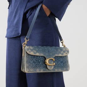 Model carrying Coach Tabby 26 Denim Embellished Shoulder Bag in denim with gold-tone C-logo hardware and floral embellishment, styled with navy outfit