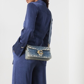 Model carrying Coach Tabby 26 Denim Embellished Shoulder Bag in gradient denim with gold-tone C-logo hardware, worn crossbody over blue suit
