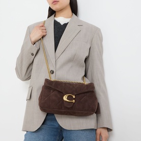 Model carrying Coach Tabby 26 Quilted Shoulder Bag in dark chocolate quilted suede with gold-tone chain strap and C-logo clasp, styled with grey