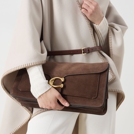 Model carrying Coach Tabby 36 Suede Shoulder Bag in Dark Chocolate with gold-tone C-logo clasp, styled with cream cape and white trousers