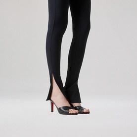 Model wearing Christian Louboutin black leather mule heels with open toe and signature red sole, styled with black slim-fit trousers