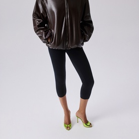 Model wearing Christian Louboutin heeled mules in kiwi green patent leather with gold-tone detailing, styled with black cropped leggings