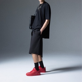 Model wearing Christian Louboutin red low-top trainers, styled with black oversized tee, shorts and socks.