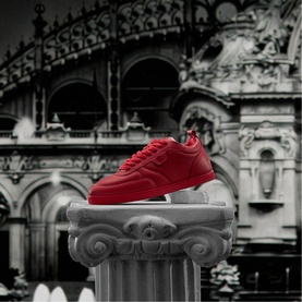Christian Louboutin red leather low-top sneaker with white chunky sole, displayed on a stone column pedestal against monochrome architectural