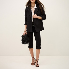 Model wearing Bash blue blazer and cropped trousers, styled with black feather clutch bag and strappy heeled sandals