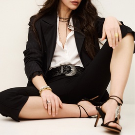 Model wearing Bash blue suit with white shirt, styled with strappy heeled sandals, gold chain bracelet, and layered necklaces.