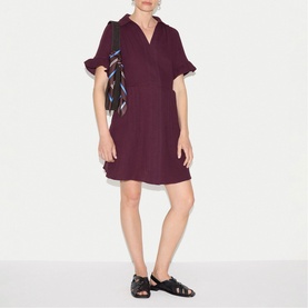 Model wearing Jigsaw purple mini dress with V-neck and ruffle sleeves, styled with black sandals and striped bag.