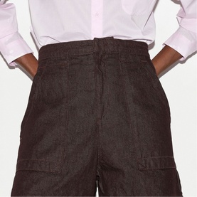 Model wearing dark brown wide-leg trousers with front patch pockets, styled with a white shirt. Close-up rear view.