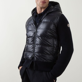 Model wearing Moncler navy cardigan with quilted down front panel, hood, and knit sleeves, paired with navy trousers.
