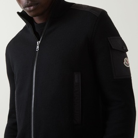 Model wearing Moncler black zip-through cardigan with cargo pocket sleeve detail, logo badge, and silver zip fastening.