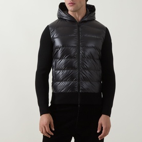 Model wearing Moncler black quilted gilet-front cardigan with hood, styled over black knit sleeves and trousers
